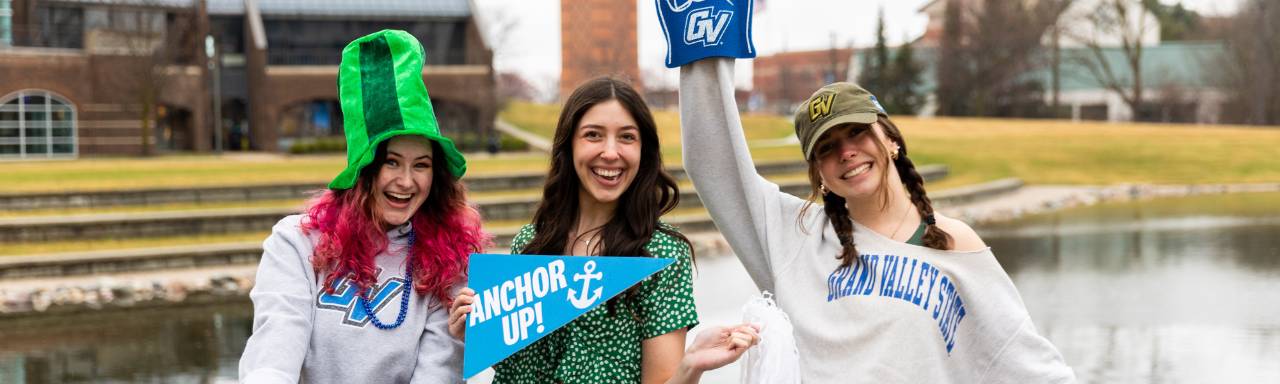A photoshoot for St. Patrick's Day giveaway with three marketing workers holding up signs that say Anchor Up and GVSU